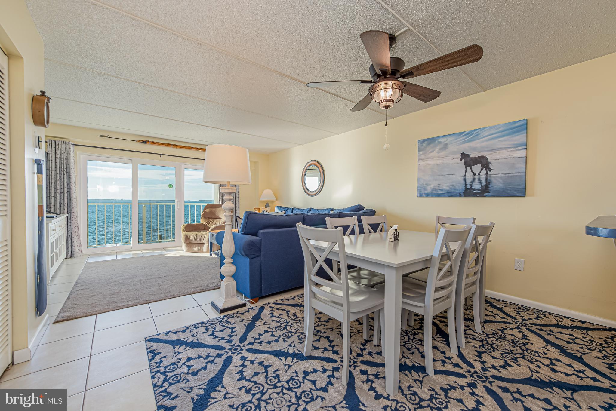 Living and dining area with blue sofas and a balcony overlooking the water.