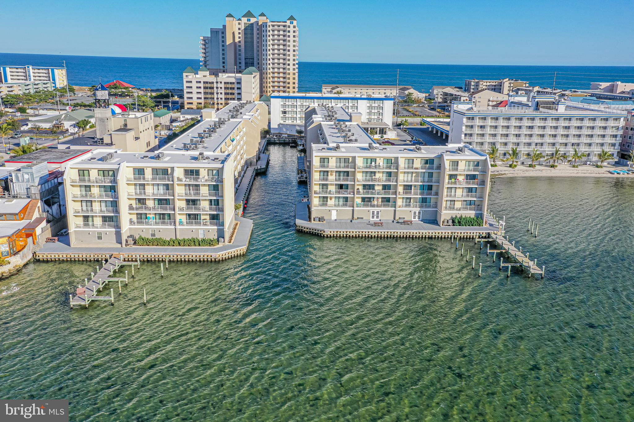 Waterfront condominiums surround a marina channel, with docks and the ocean beyond.