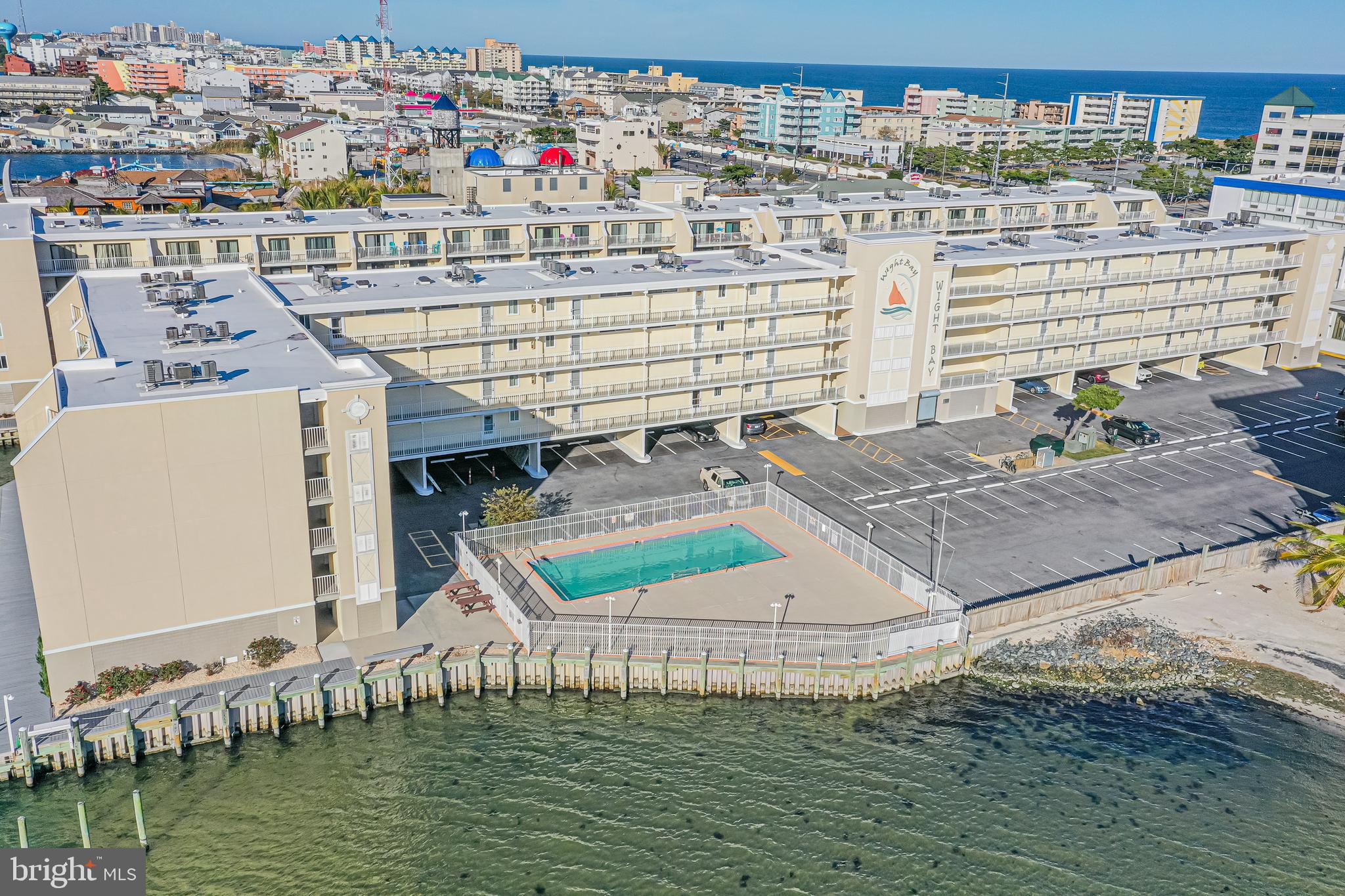 Wight Bay condominium building with a waterfront pool, parking, and Ocean City’s oceanfront skyline beyond.