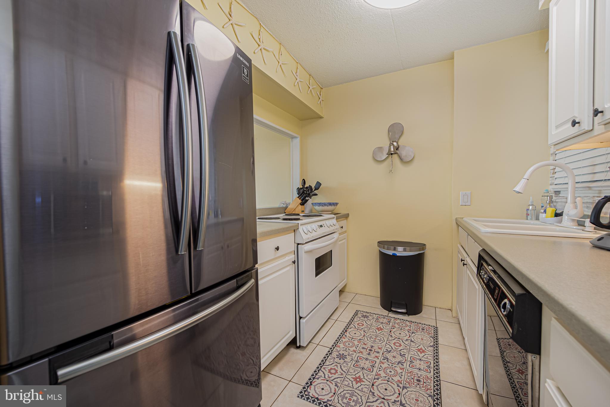 Kitchen with stainless-steel refrigerator, white appliances, and a colorful patterned runner.
