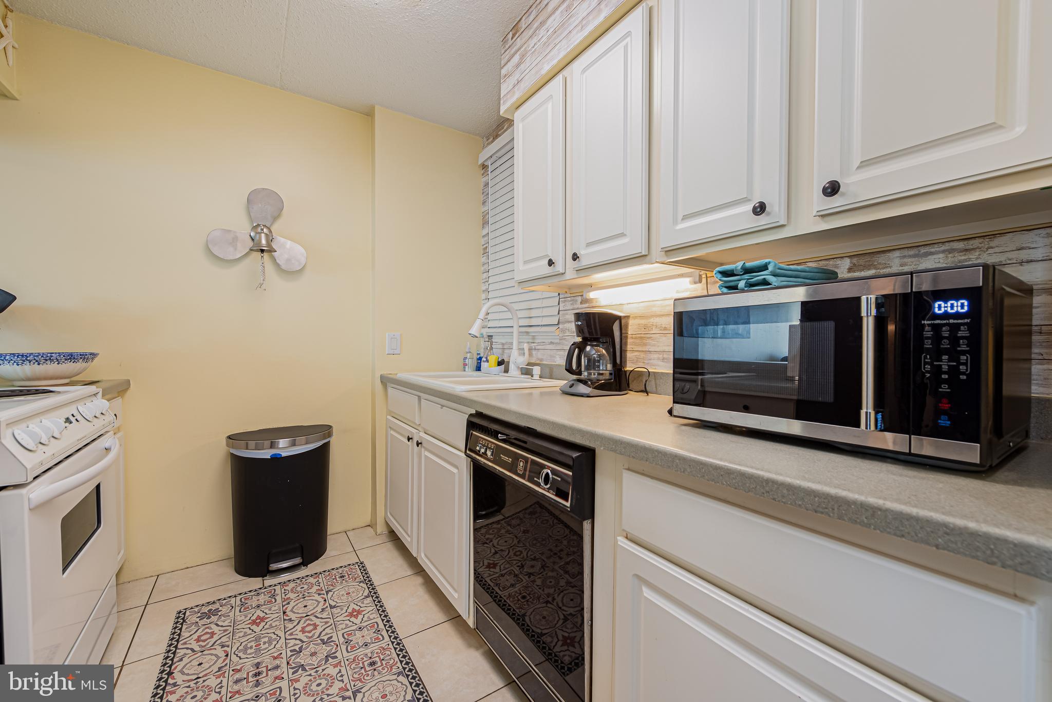 Condo kitchen with white cabinets, stainless microwave, and patterned floor runner.