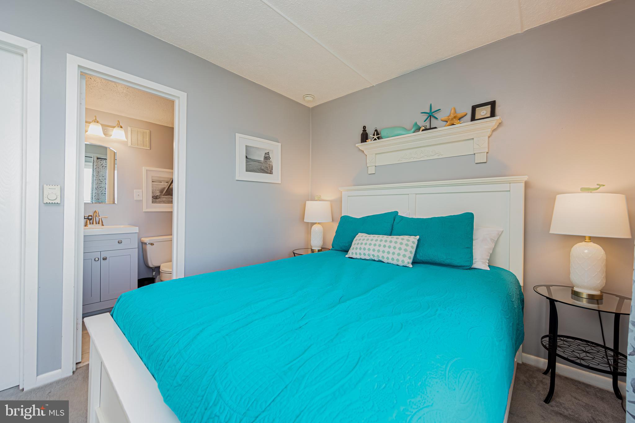 Bedroom with vivid turquoise bedding, white headboard, and coastal decorations above the bed.