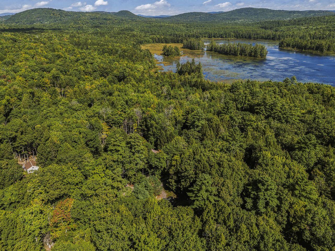 Aerial view of a forested property beside a lake, with wooded islands and distant hills.