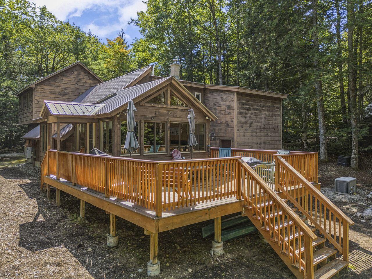 Wood-sided home with a raised deck, outdoor seating, and metal roof, surrounded by trees.