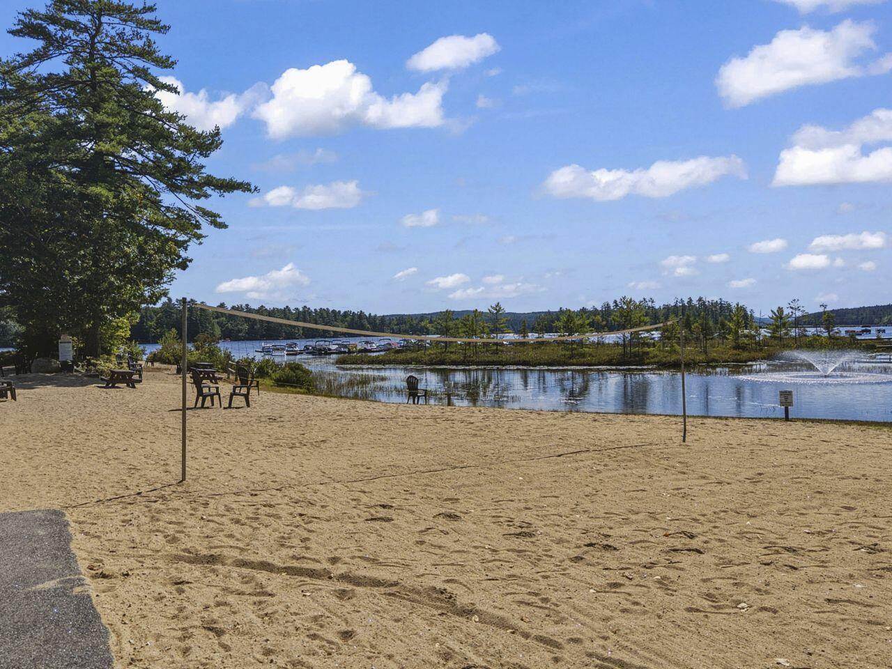 Sandy lakeside beach with a volleyball net, Adirondack chairs, and a fountain.