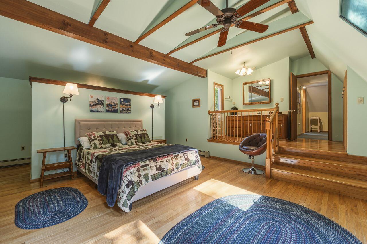 Bedroom with exposed ceiling beams, hardwood floors, and a raised landing with a wooden railing.
