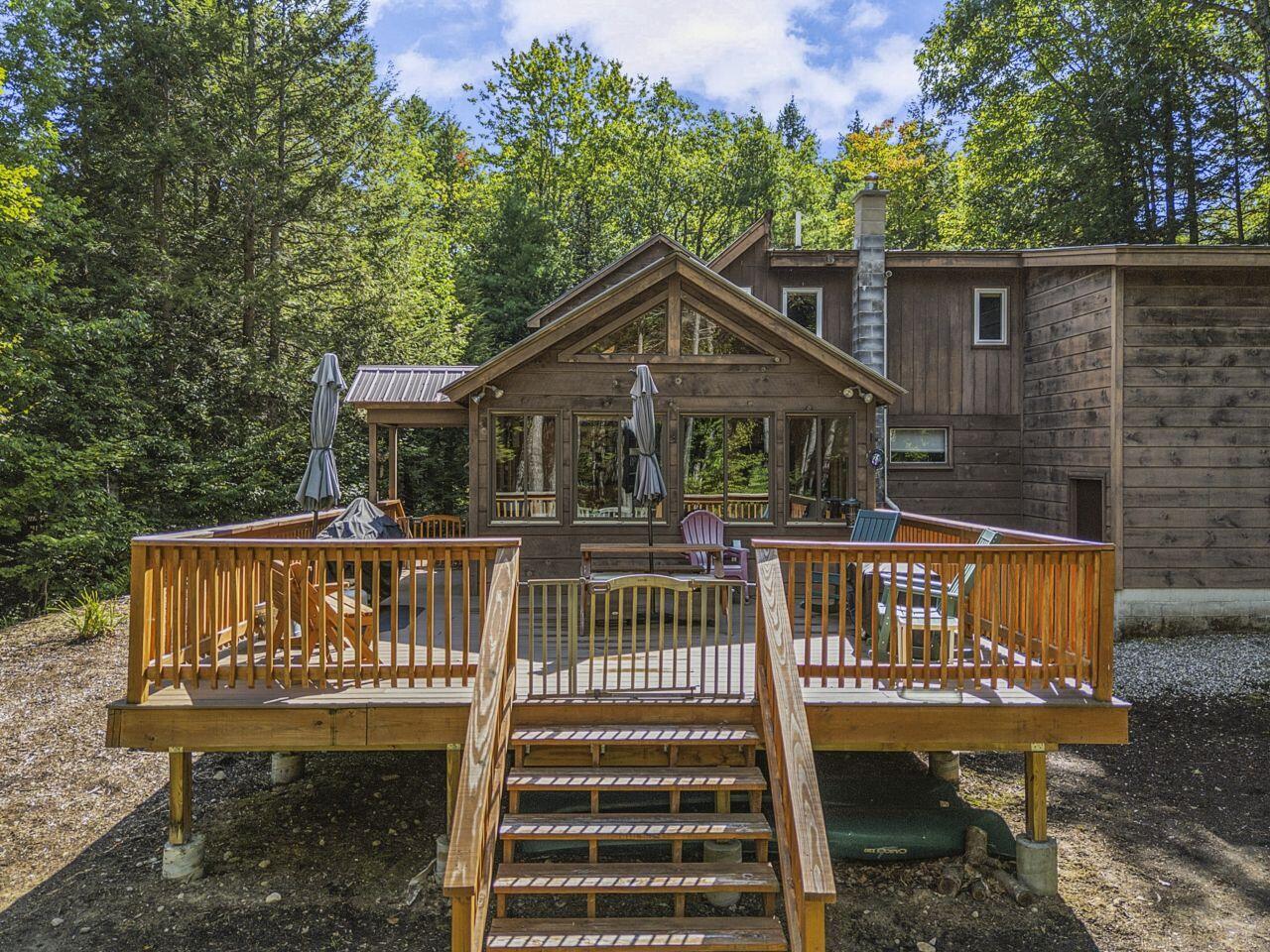 Wood-sided home with a raised deck and central stairs, surrounded by trees.