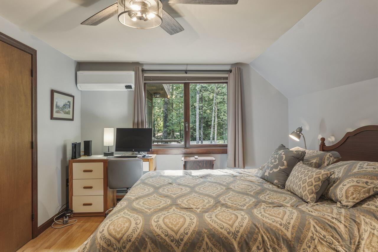 Bedroom with a patterned bed and desk beside a window overlooking trees.