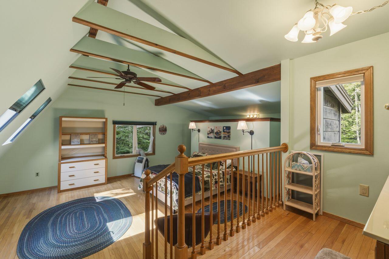 Furnished loft bedroom with exposed ceiling beams, hardwood floors, and a wooden railing around the bed area.