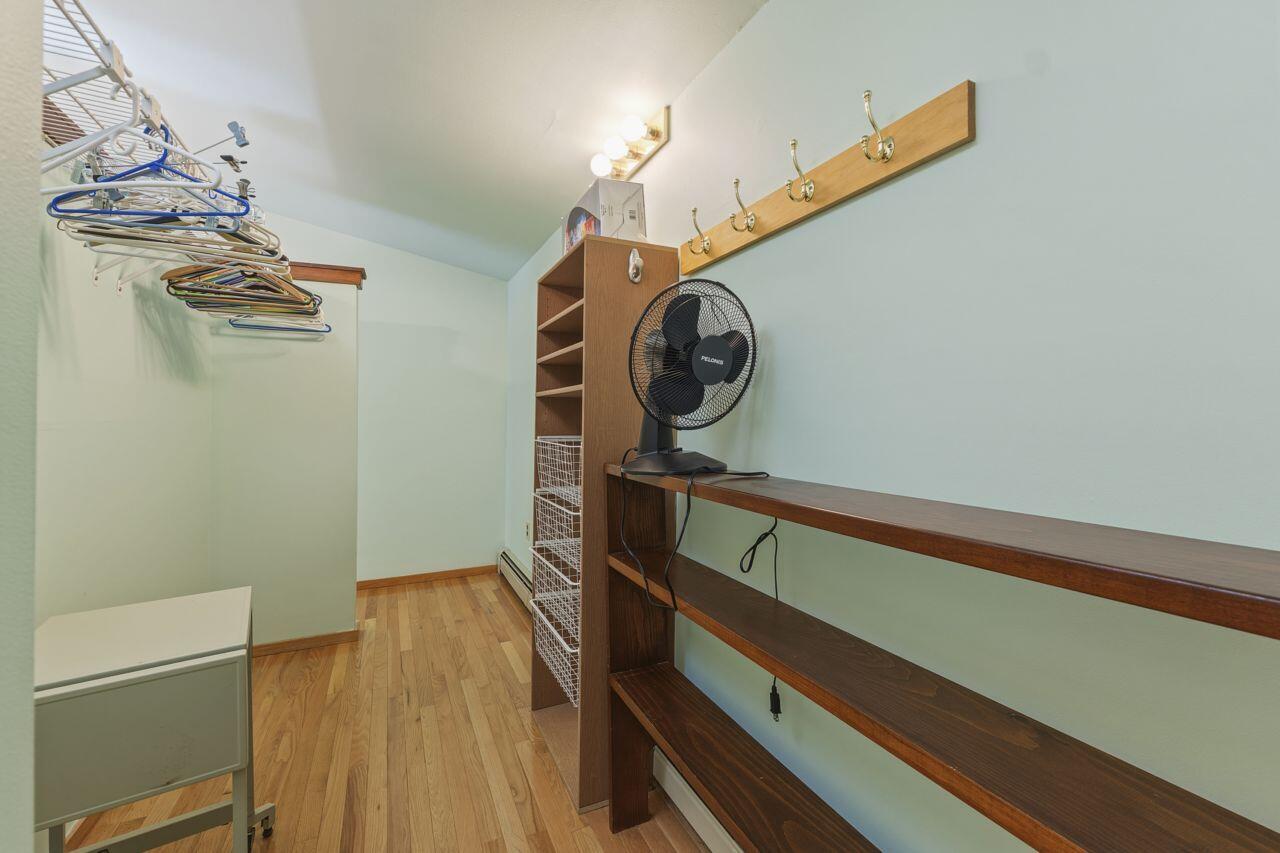 Walk-in closet with clothes rails, wooden shelving, wire baskets, and a standing fan.