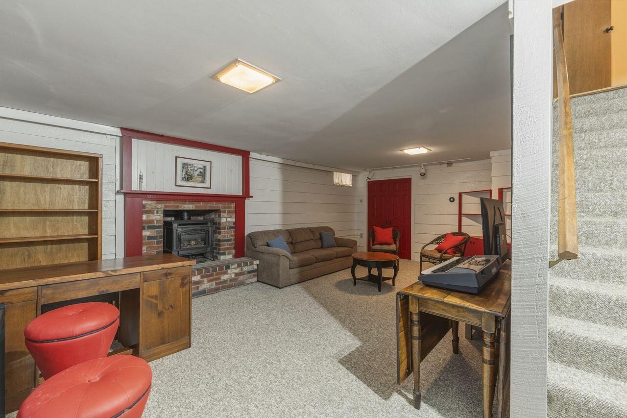 Basement recreation room with a brick fireplace, red trim, built-in shelving, and carpeted floor.