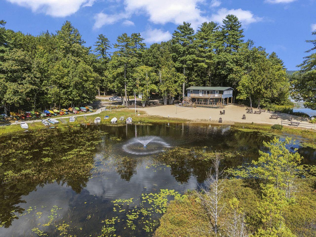 Waterfront property with a sandy beach, kayaks, and a fountain in the pond.