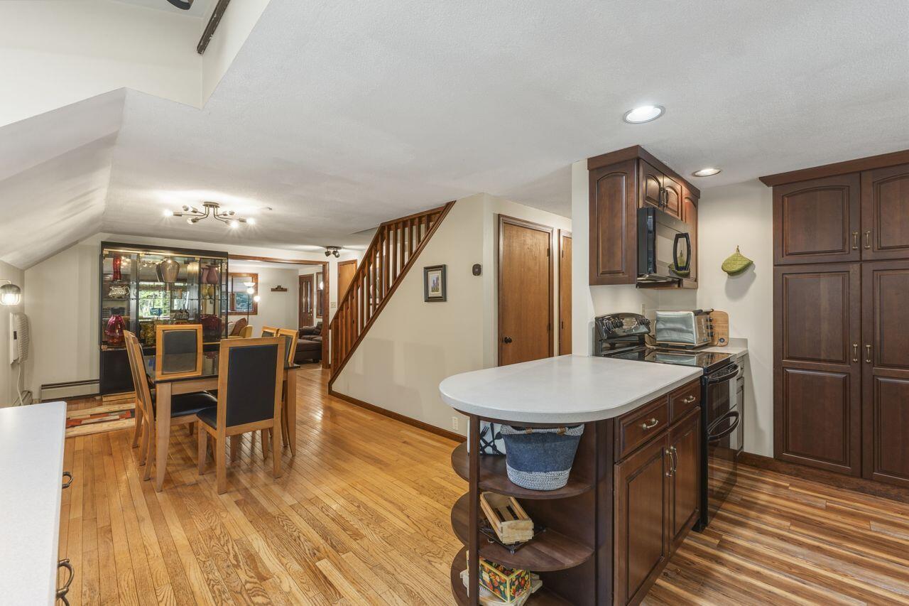 Kitchen and dining area with a white island, dark wood cabinets, hardwood floors, and a staircase.