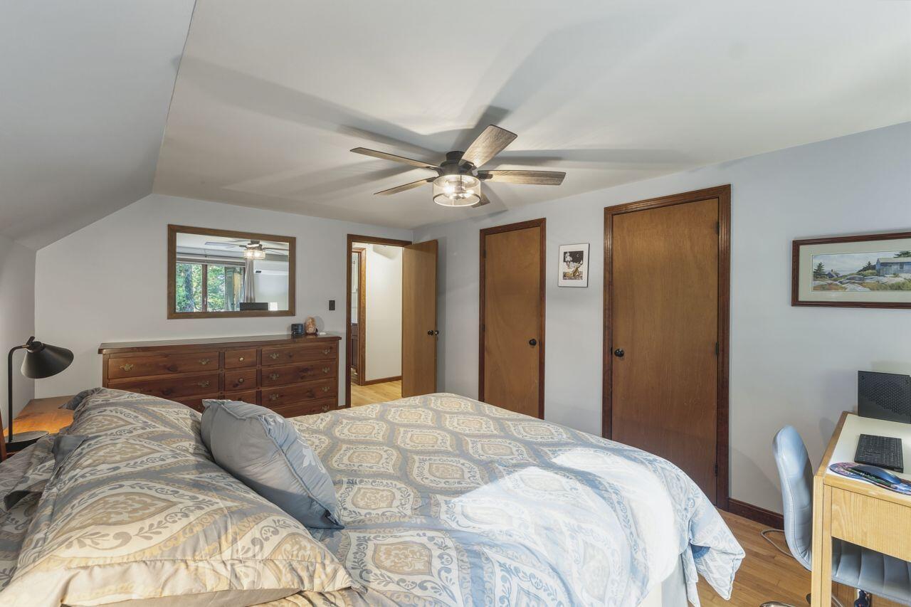 Furnished bedroom with a patterned bed, wooden dresser, ceiling fan, and hardwood floor.