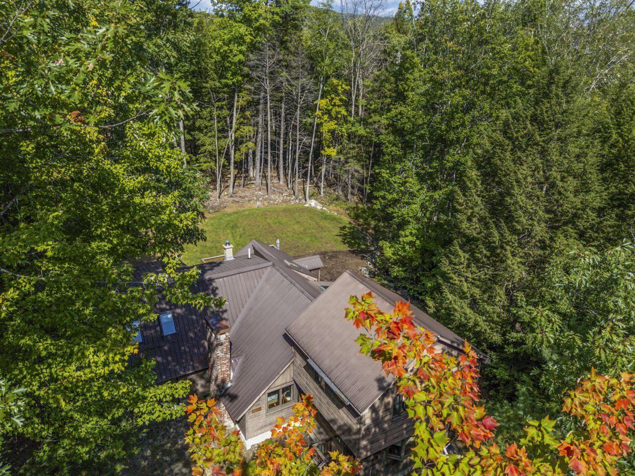 Aerial view of a wooded house with a metal roof and a grassy clearing.