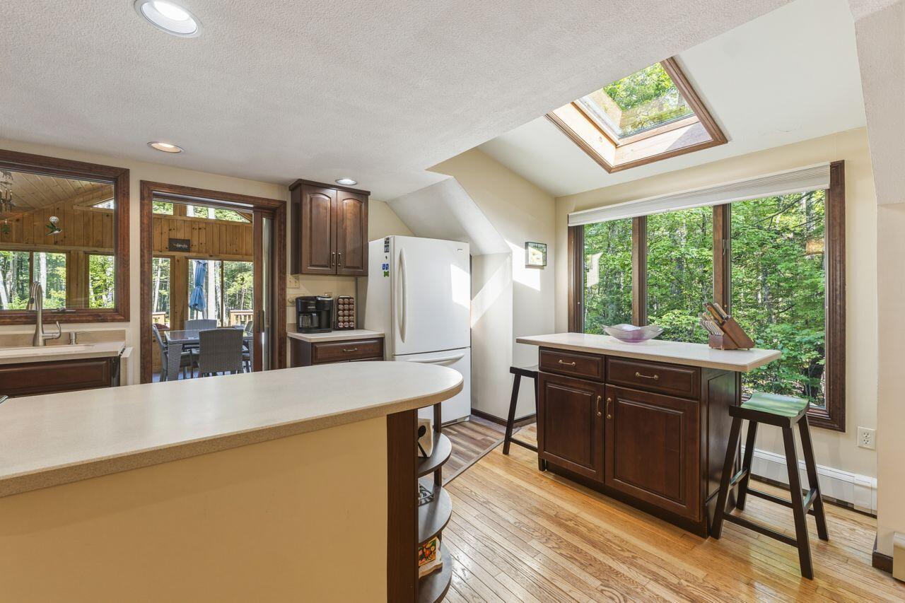 Kitchen with a large peninsula, dark wood cabinets, skylight, and windows overlooking trees.