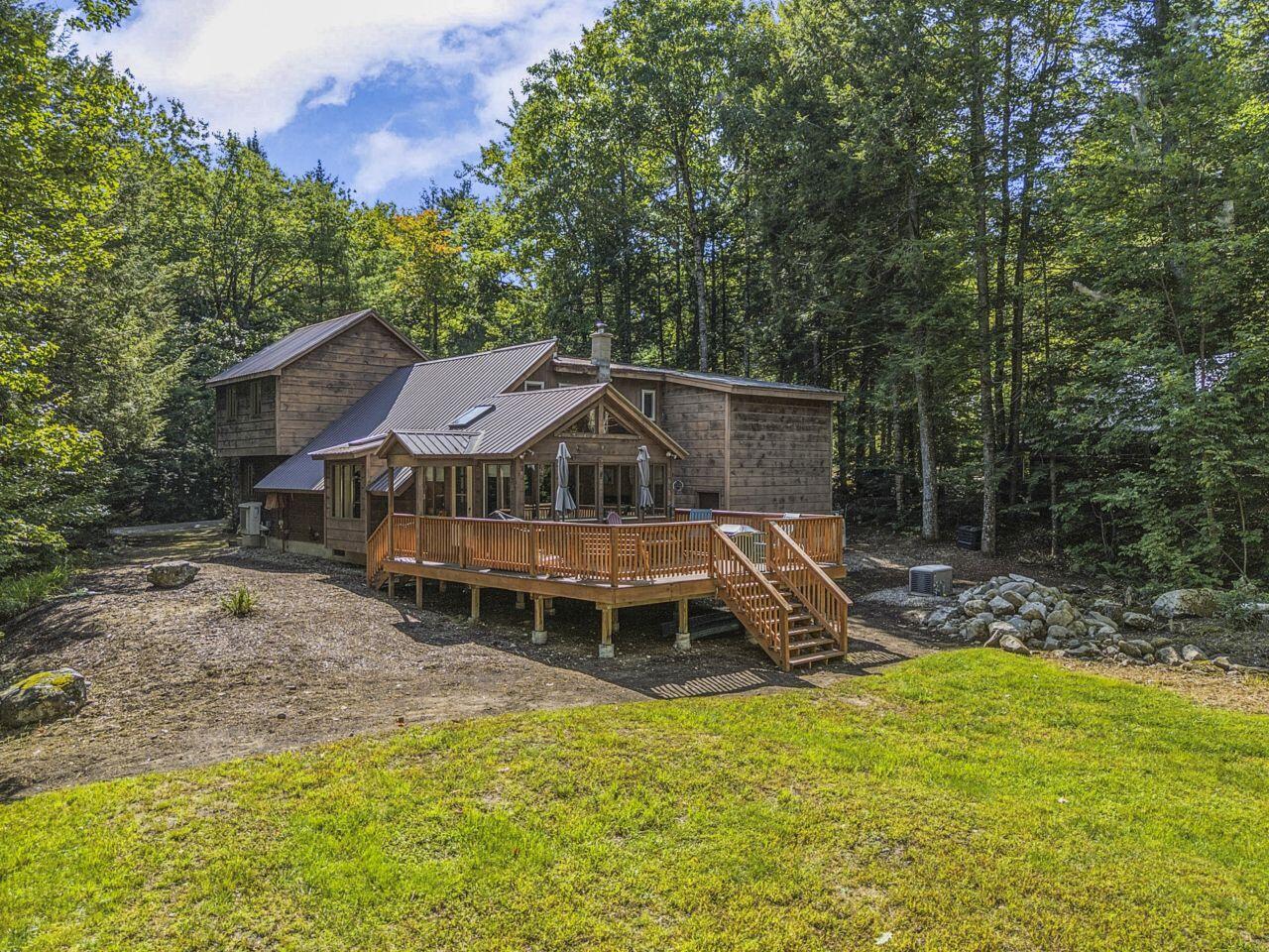 Multi-level wood-sided home with a raised deck, surrounded by mature trees.