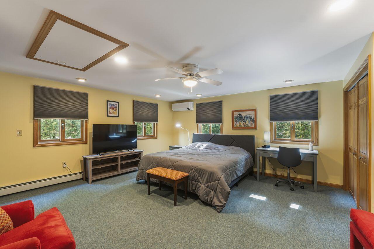 Spacious bedroom with a large bed, wood-trimmed windows, dark blinds, and a desk.