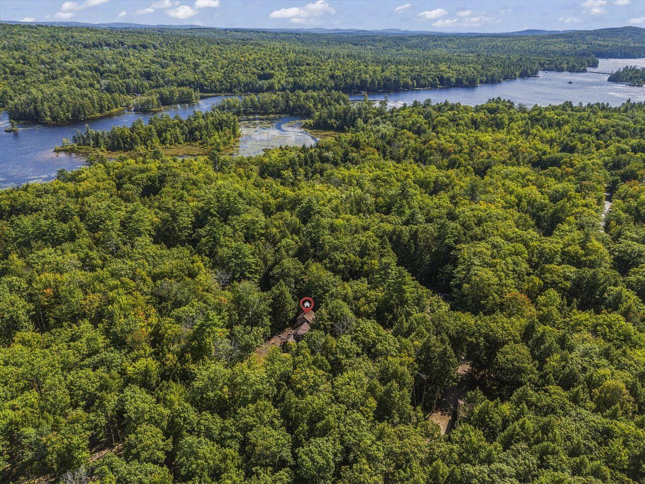 Wooded property beside a winding lake, with a small home tucked among trees.