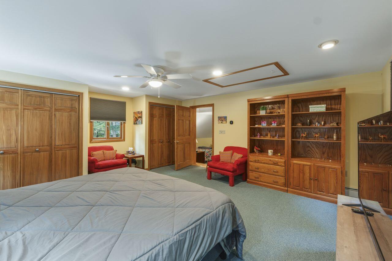 Bedroom with a large bed, wooden built-ins, red armchairs, and a ceiling fan.