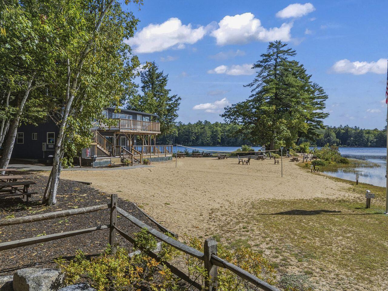 Lakeside building beside a sandy beach with a wooden deck, picnic tables, and volleyball net.