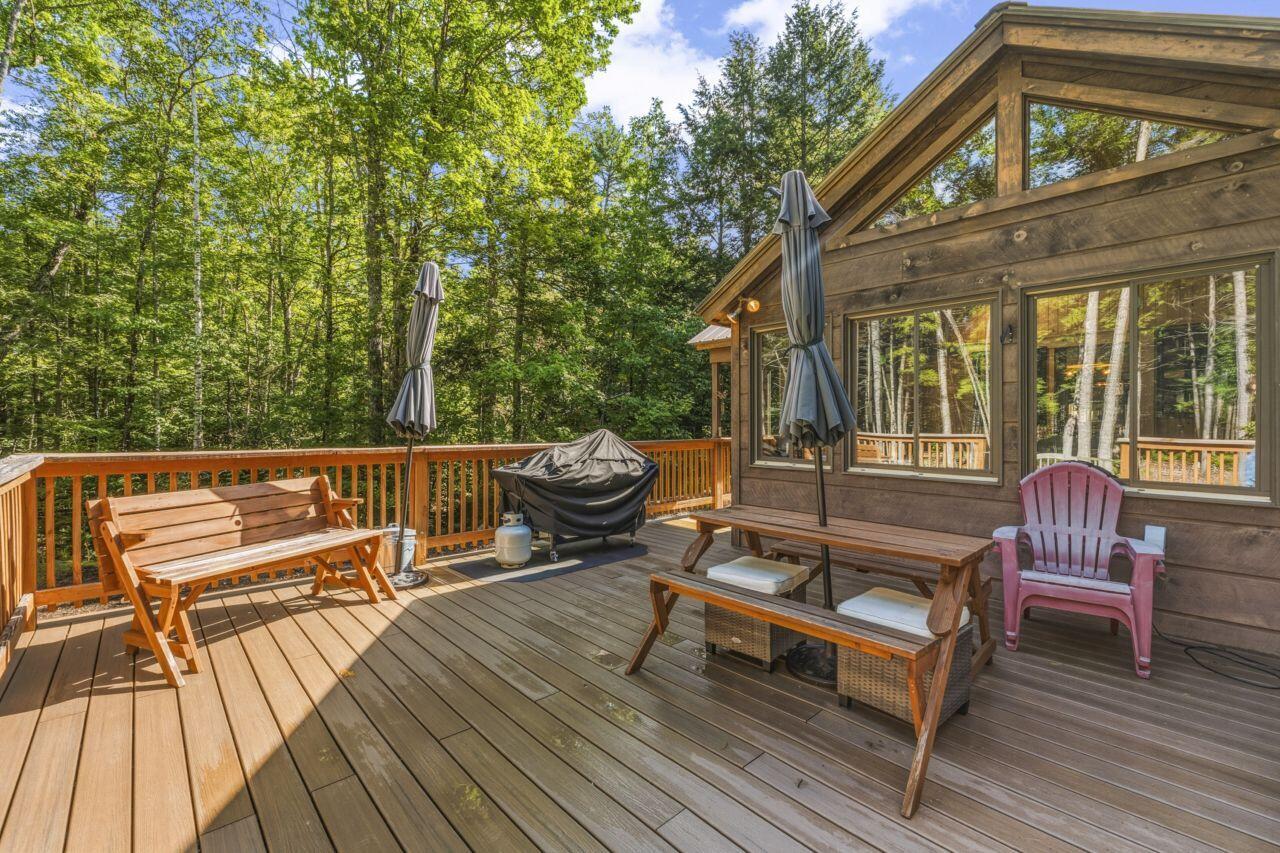 Wooden deck with outdoor seating and a covered grill, surrounded by leafy trees.