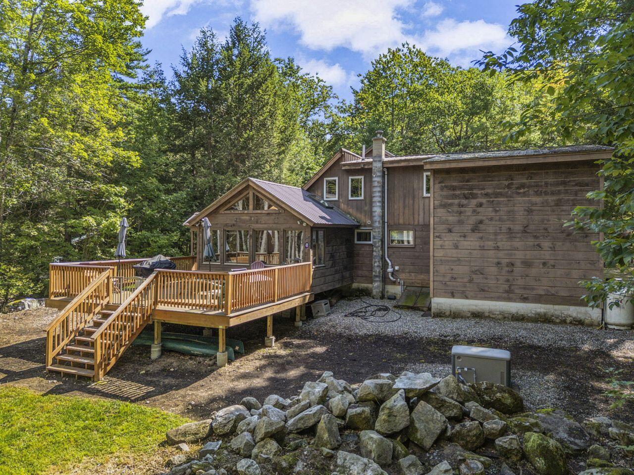 Wood-sided home with a raised deck and glass-fronted porch surrounded by trees.