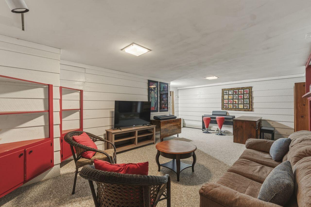 Furnished recreation room with a brown sectional, red-cushioned wicker chairs, television, and keyboards.