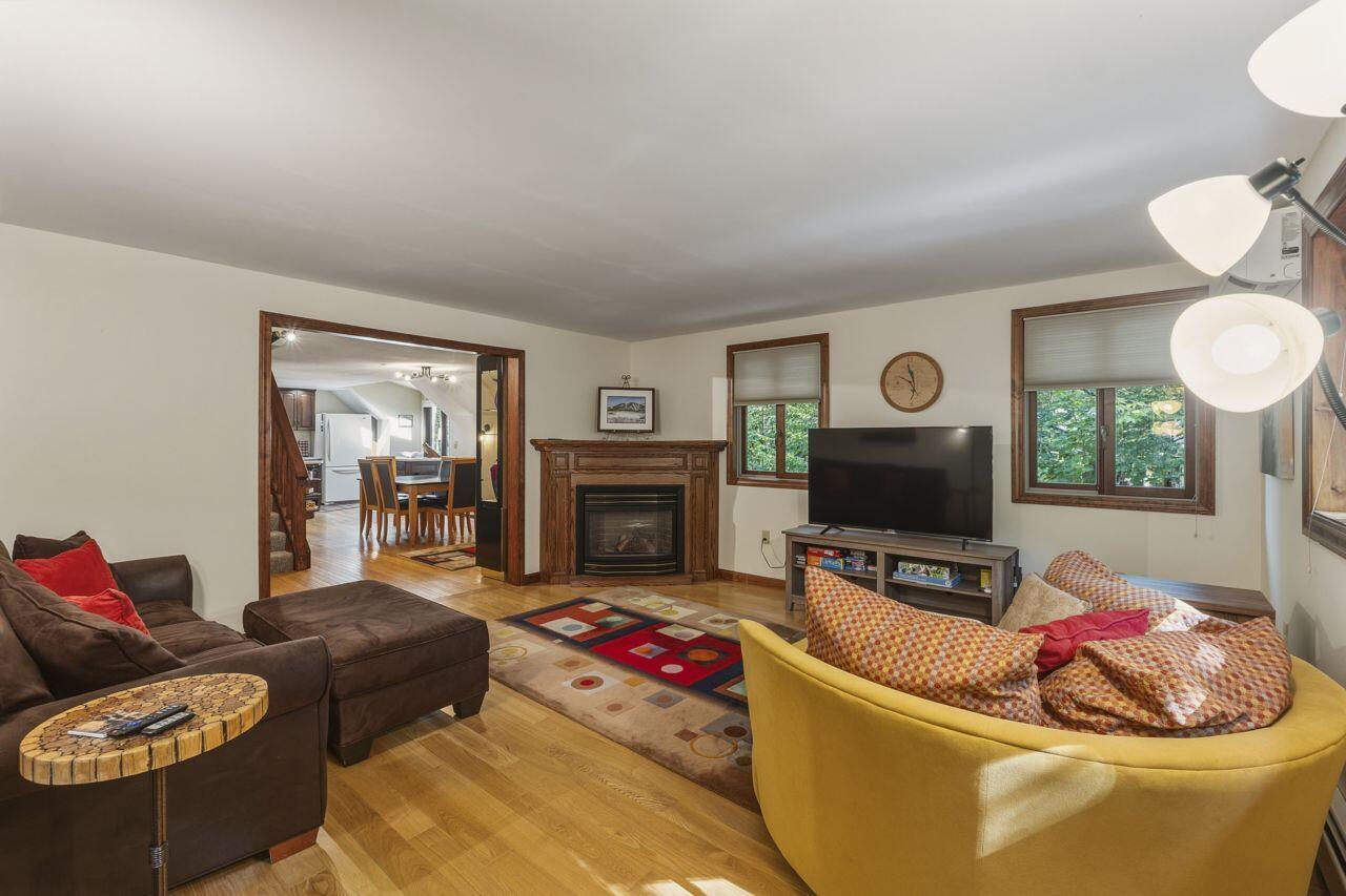 Living room with a wood-trimmed fireplace, colorful seating, hardwood floors, and an adjoining dining area.