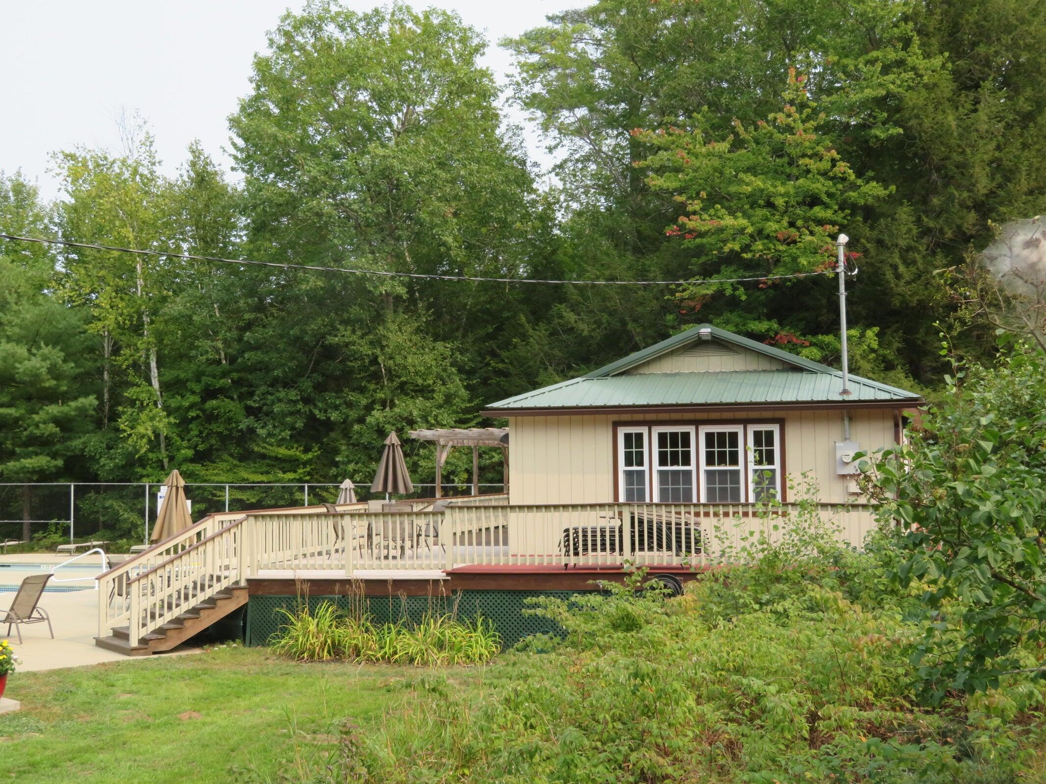Poolside building with a raised deck beside a swimming pool, surrounded by trees.