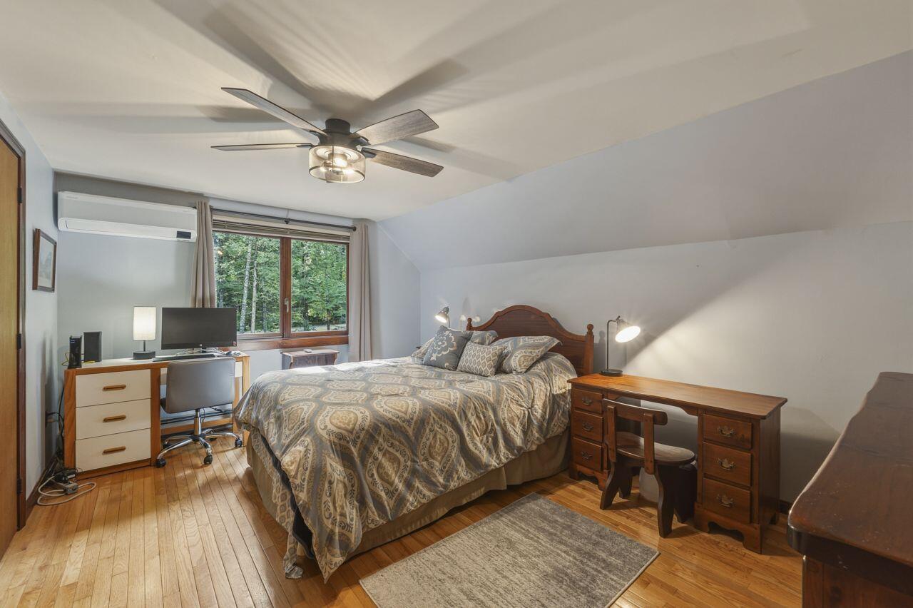 Bedroom with patterned bedding, hardwood floors, and a large window overlooking trees.