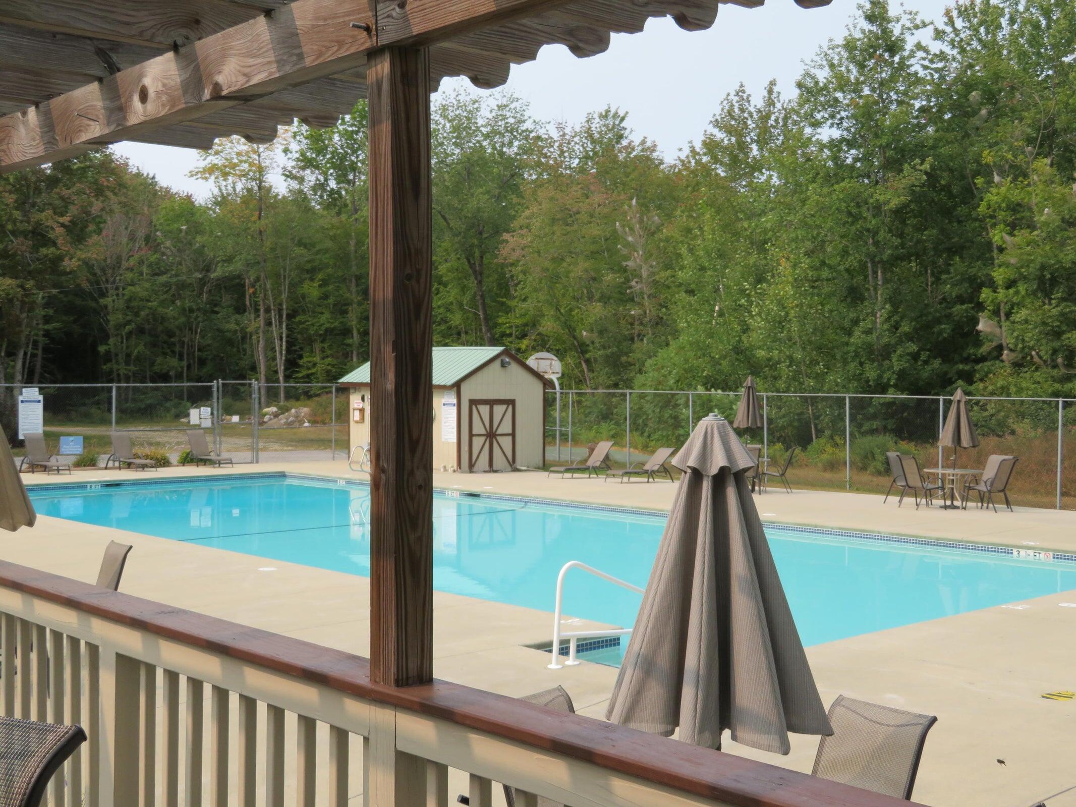 Outdoor swimming pool with a fenced deck, lounge chairs, and wooded surroundings.
