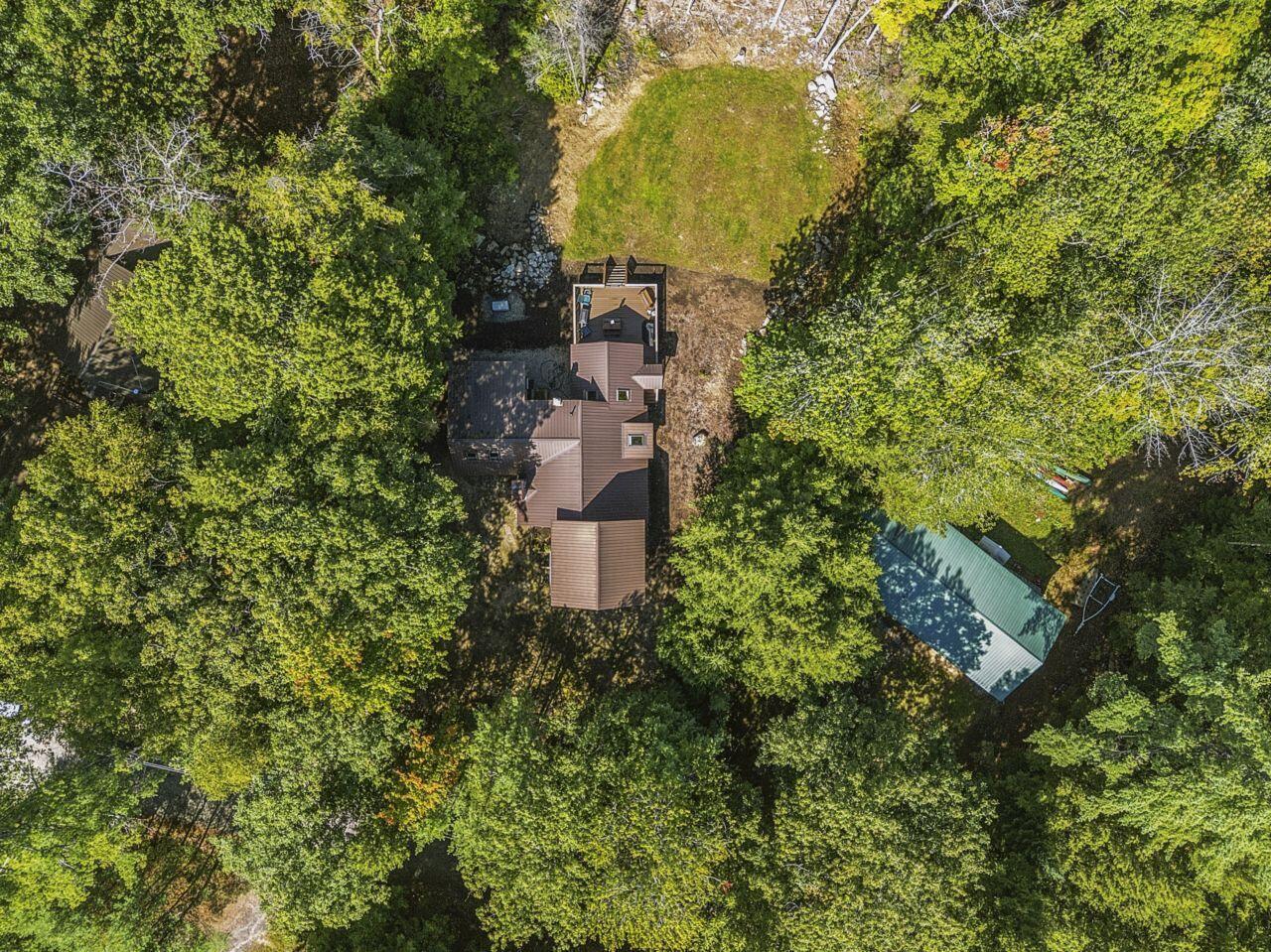 Aerial view of a house nestled among dense trees beside a grassy clearing.
