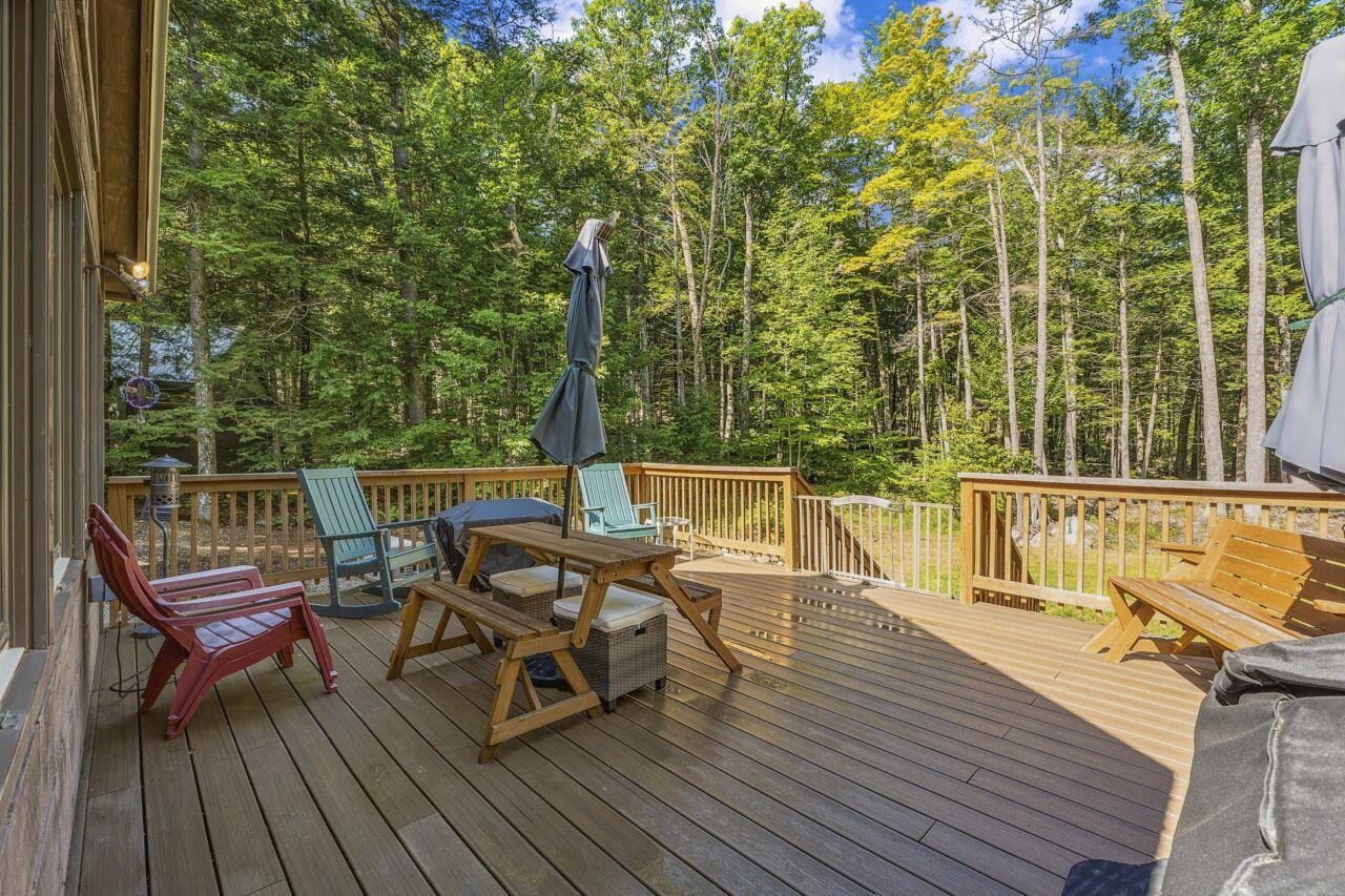 Wooden deck furnished with Adirondack chairs and a picnic table, surrounded by trees.