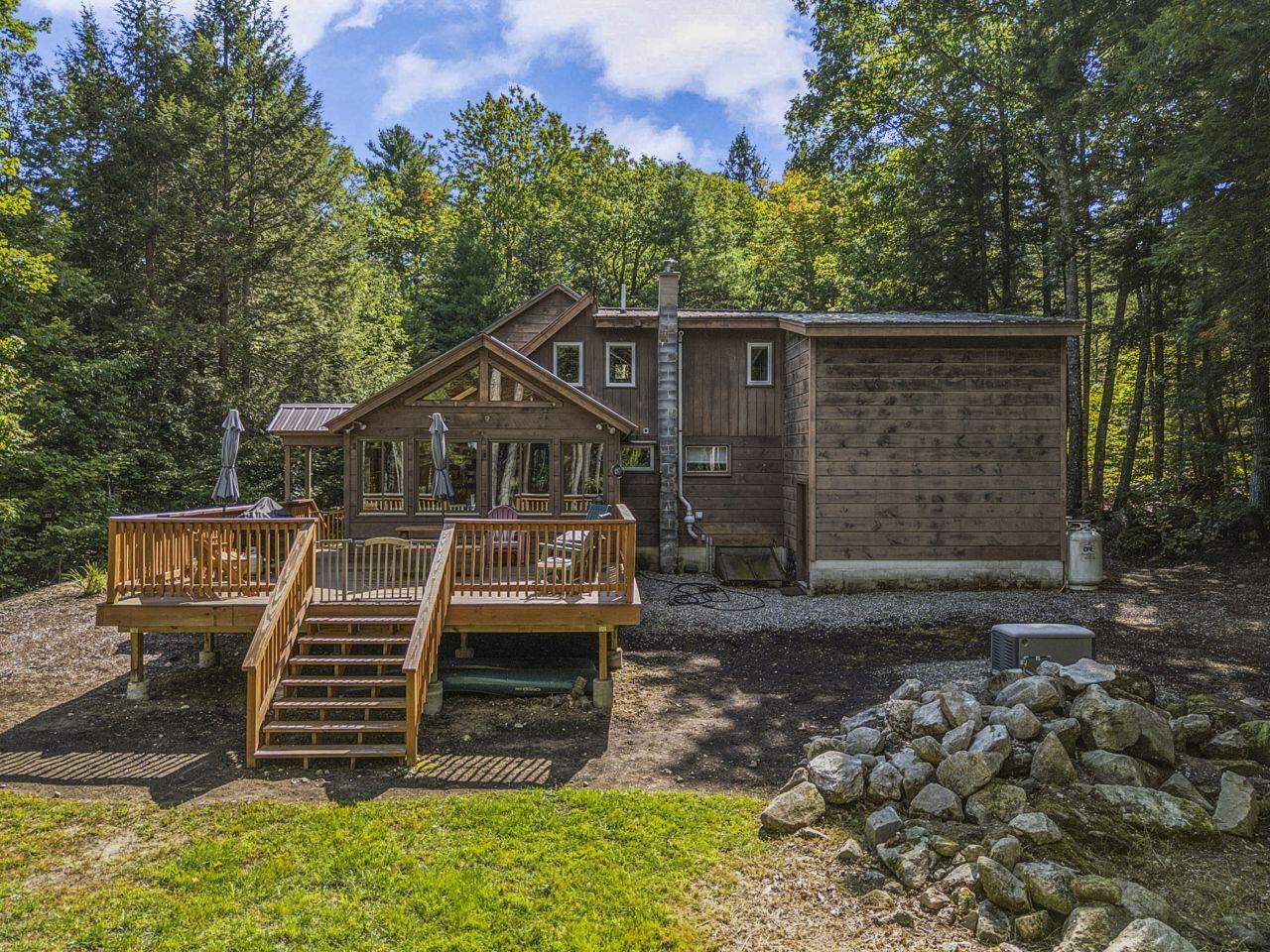 Wood-sided house with a raised deck and broad staircase, surrounded by trees and rocks.
