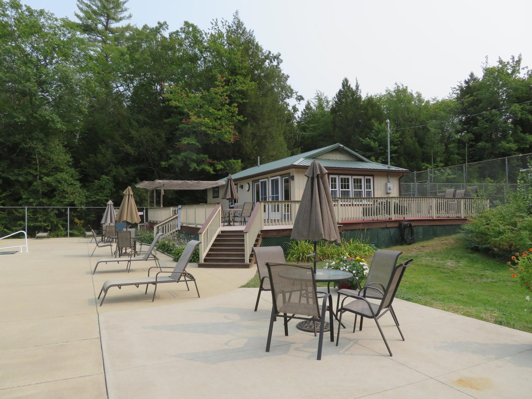 Wooded home with a raised deck and furnished concrete pool patio.