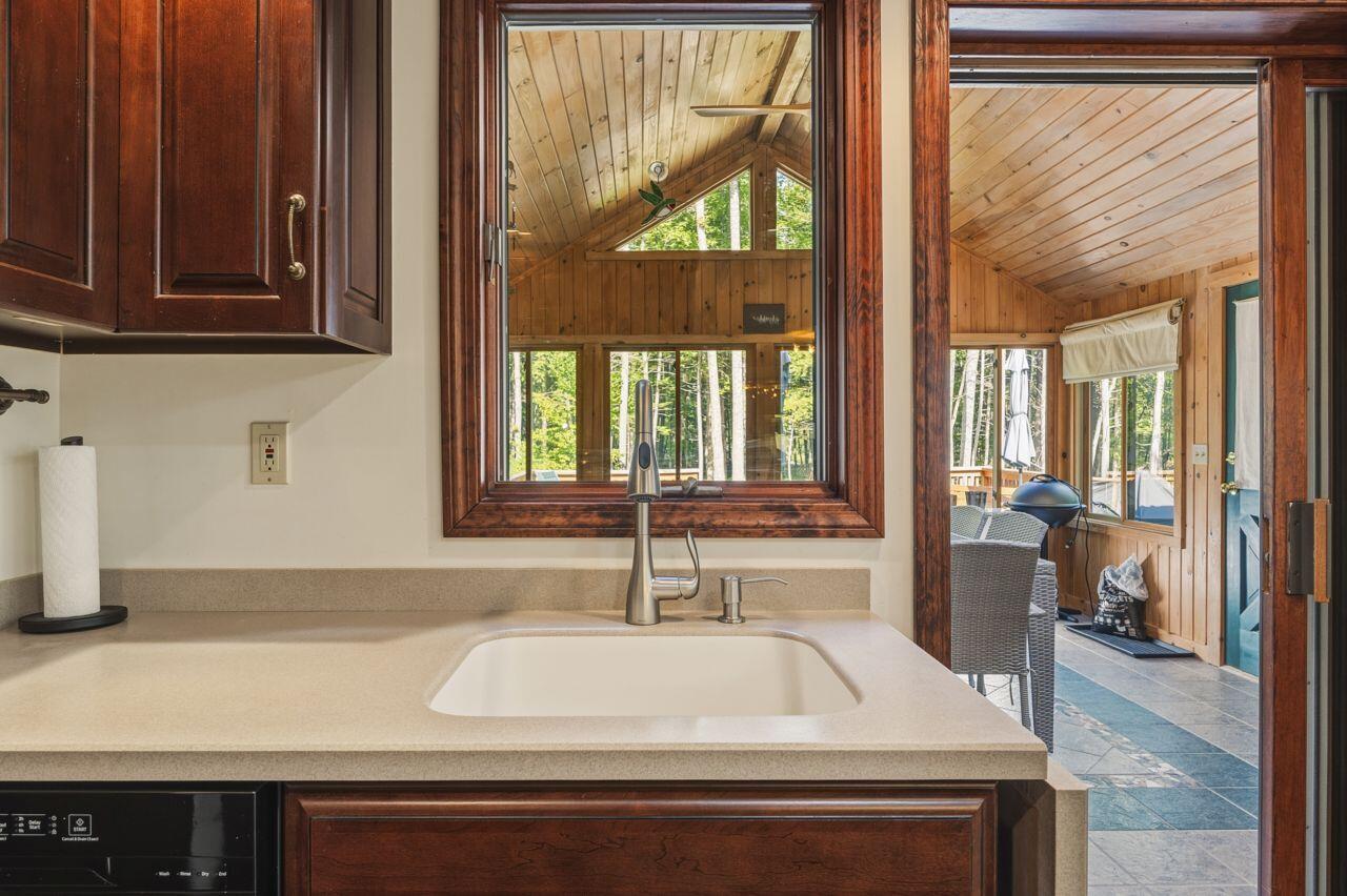 Kitchen sink and dark wood cabinets open to a wood-paneled sunroom with a vaulted ceiling.