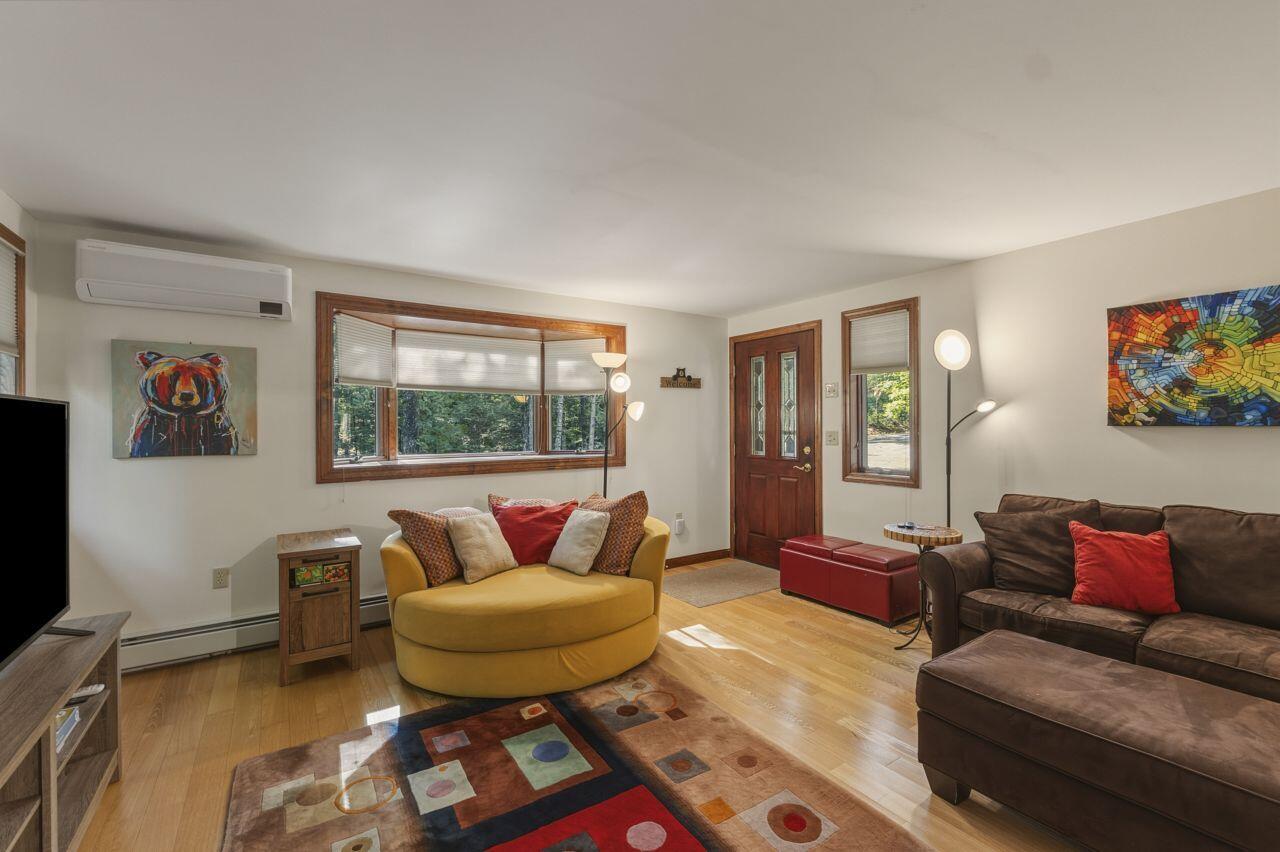 Living room with a mustard-yellow loveseat, brown sectional, colorful rug, and wide window overlooking trees.