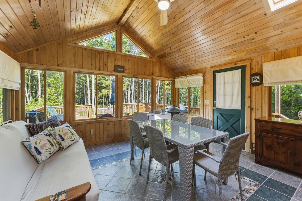 Wood-paneled sunroom with vaulted ceiling, forest-facing windows, dining table, and white sofa.