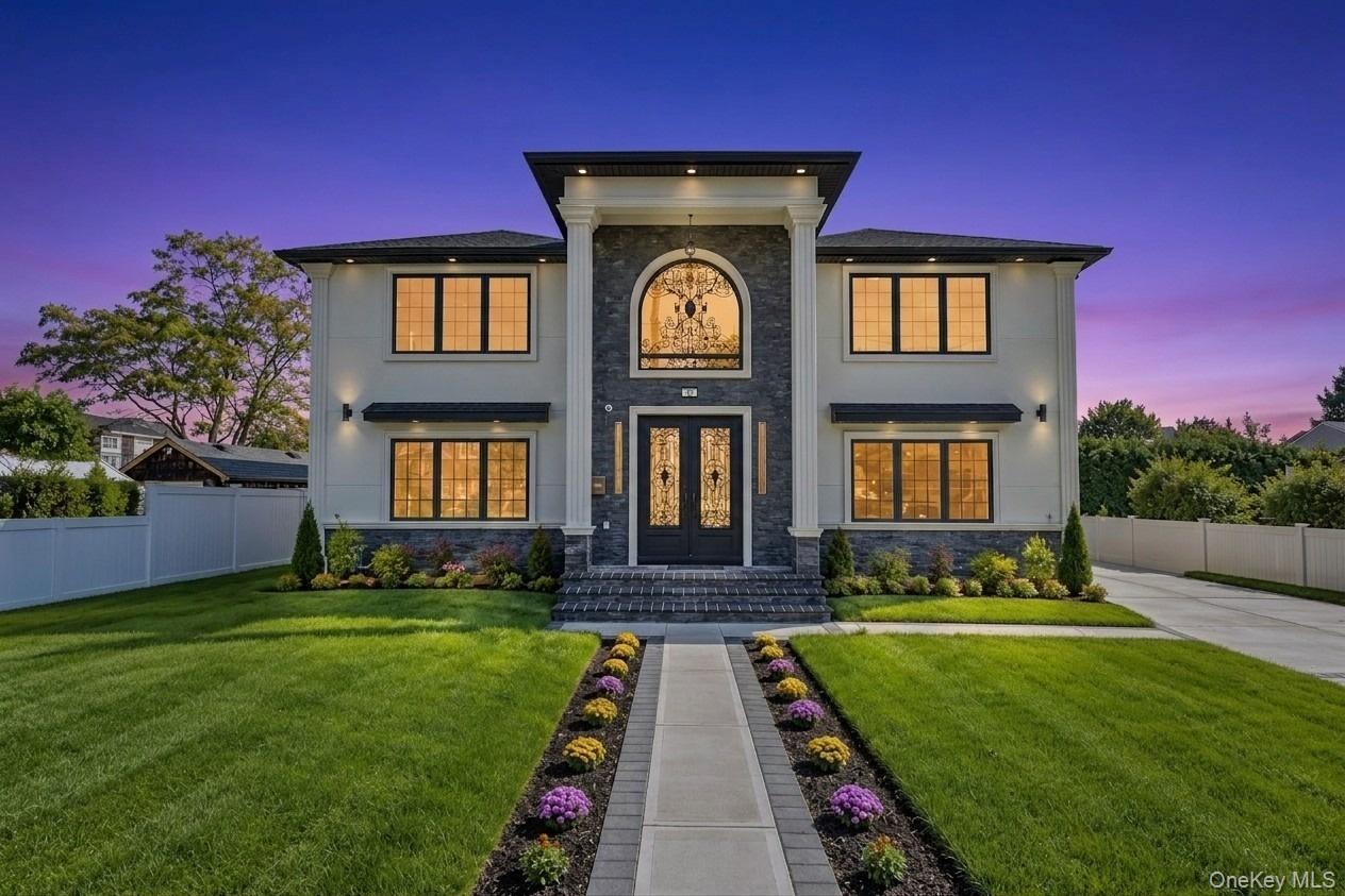 Two-story luxury home with ornate glass entry doors and a flower-lined walkway at dusk.