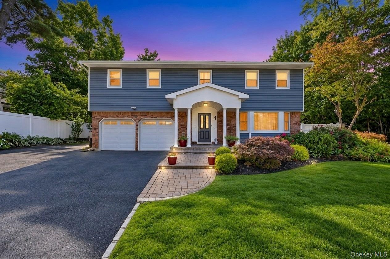 Two-story blue-and-brick home with a two-car garage, white entry portico, and landscaped front yard at dusk.