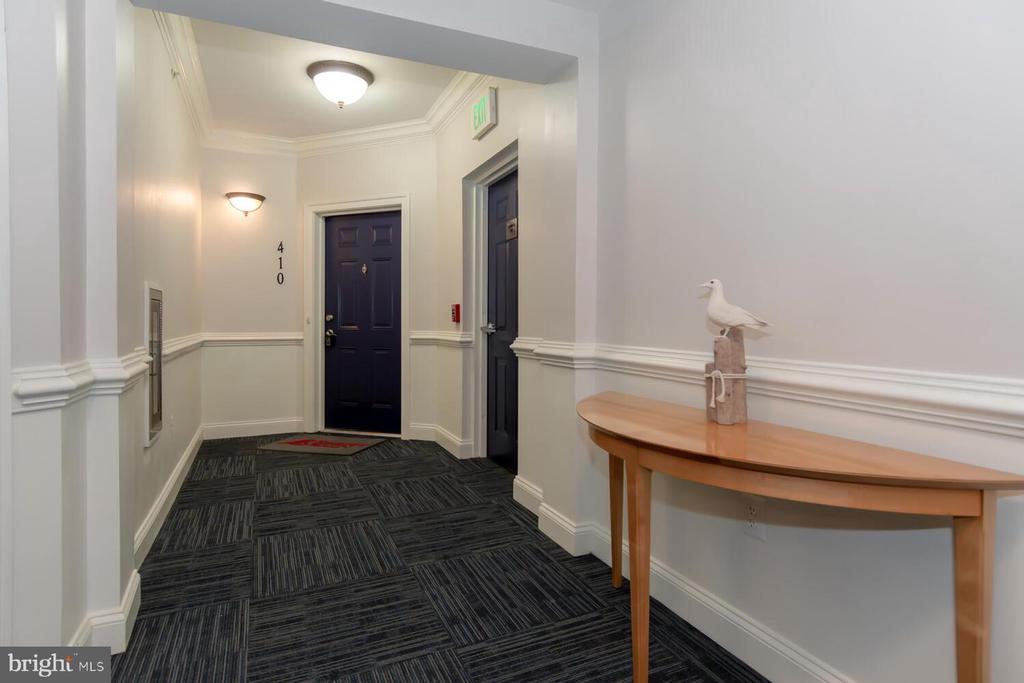Residential hallway with dark apartment doors, patterned carpet, and a wooden console table with a bird sculpture.