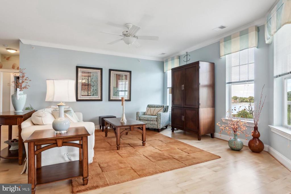 Furnished living room with a white sofa, tan rug, and tall windows overlooking the water.