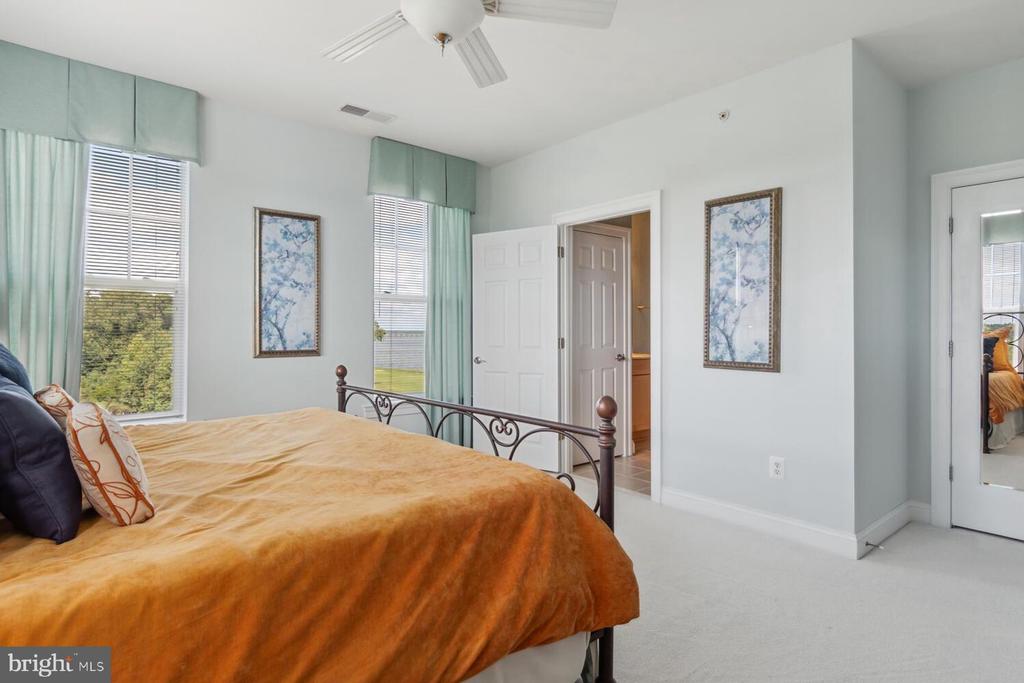 Bedroom with a metal bed, rust-orange coverlet, aqua curtains, and two windows.