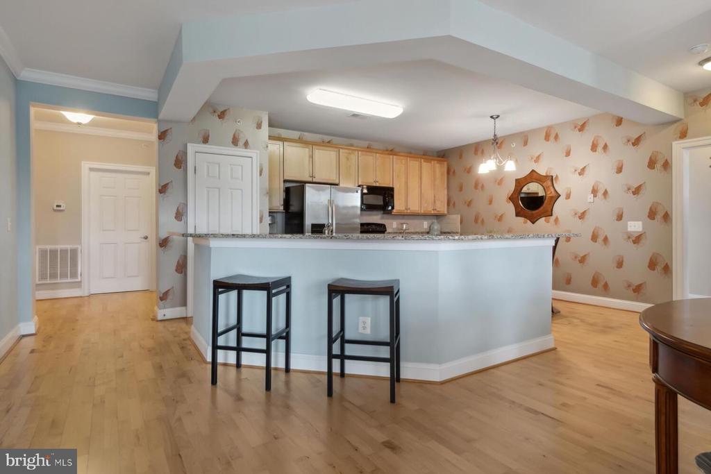 Open kitchen with light wood cabinets, stainless steel appliances, and a pale blue breakfast bar with two stools.