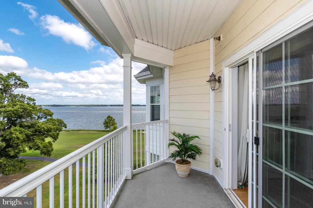 Covered balcony overlooking a broad water view, with white railings and a potted plant.