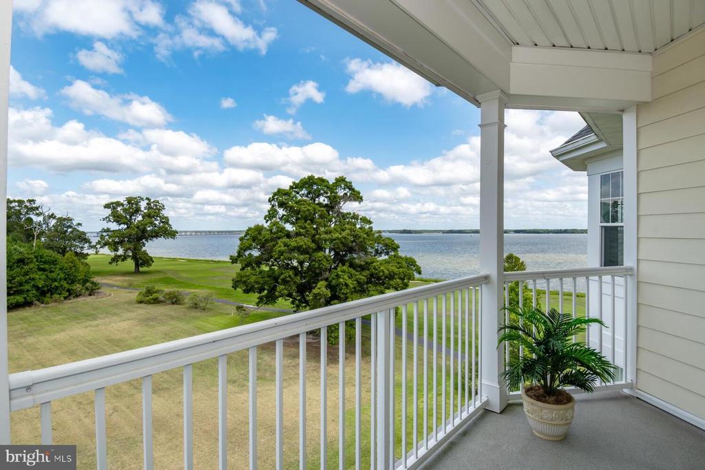 Covered balcony overlooking water and a broad lawn, with a potted plant beside the railing.