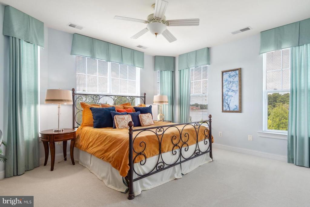 Bedroom with a wrought-iron bed, golden-orange coverlet, aqua curtains, and multiple windows.
