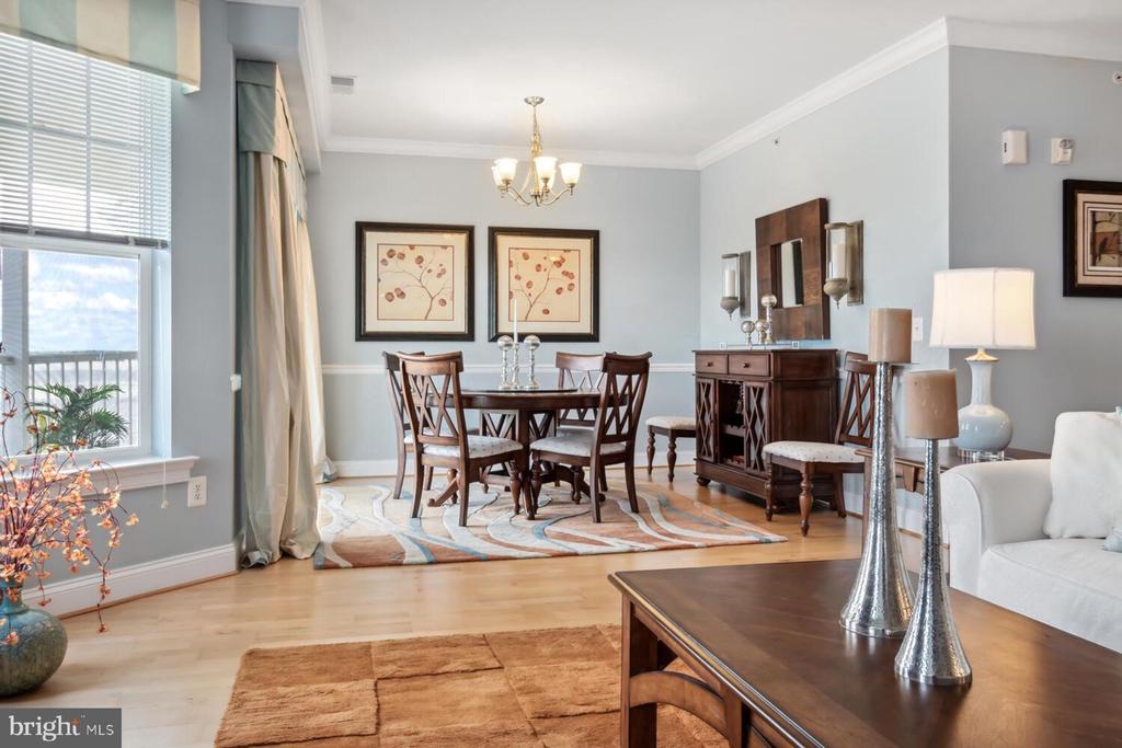 Dining area with a round table, botanical prints, and a large window overlooking a balcony.