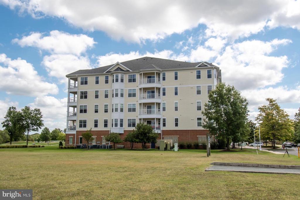Beige multi-story condominium building with balconies and a broad front lawn.
